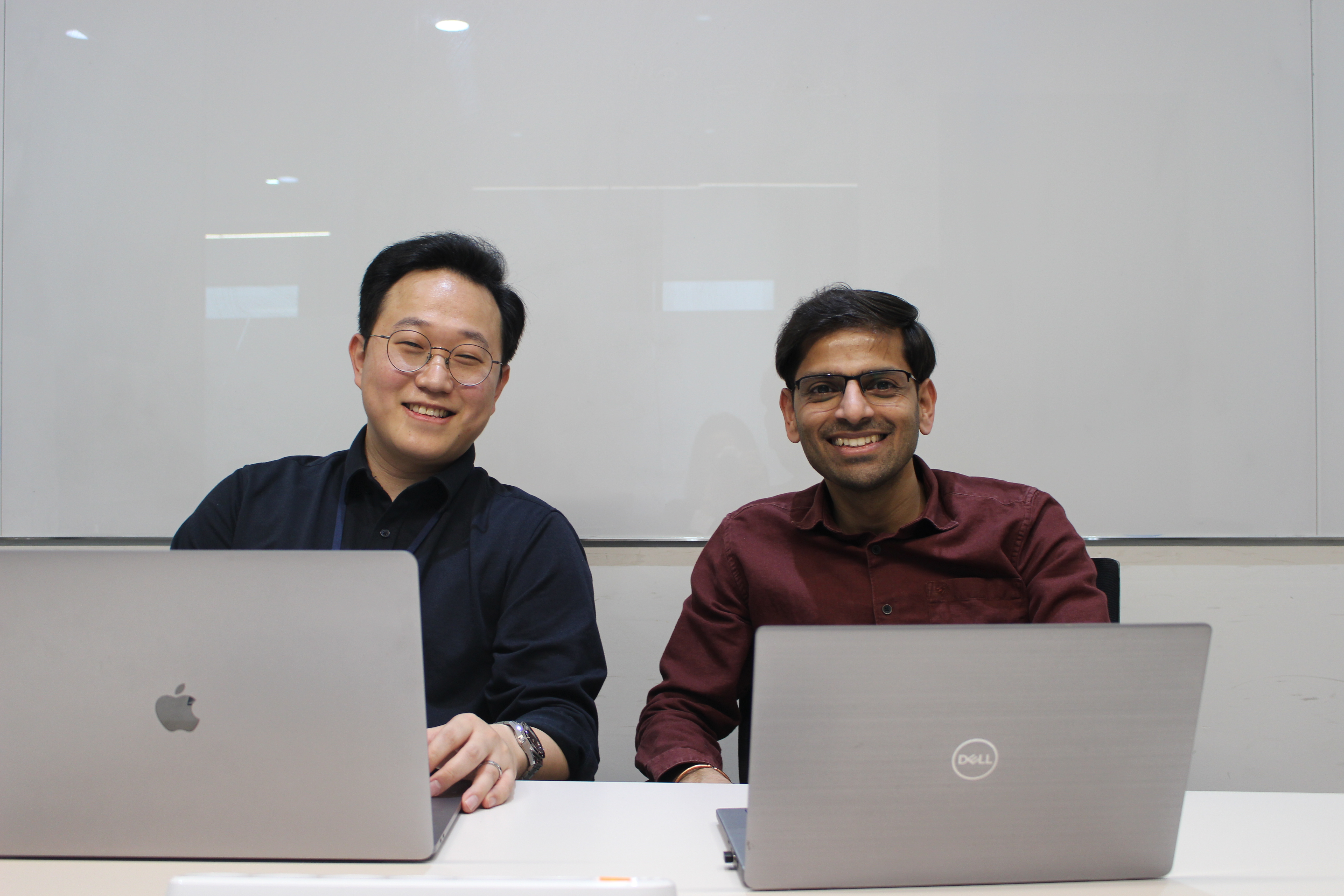 two men sitting at a table with laptops