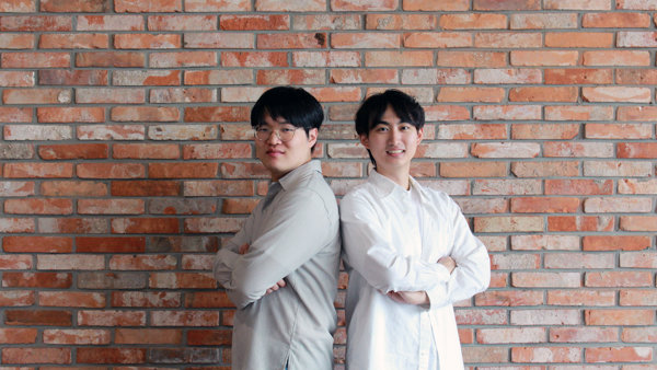 벽돌 벽 앞에 등을 맞대고 서 있는 두 남자