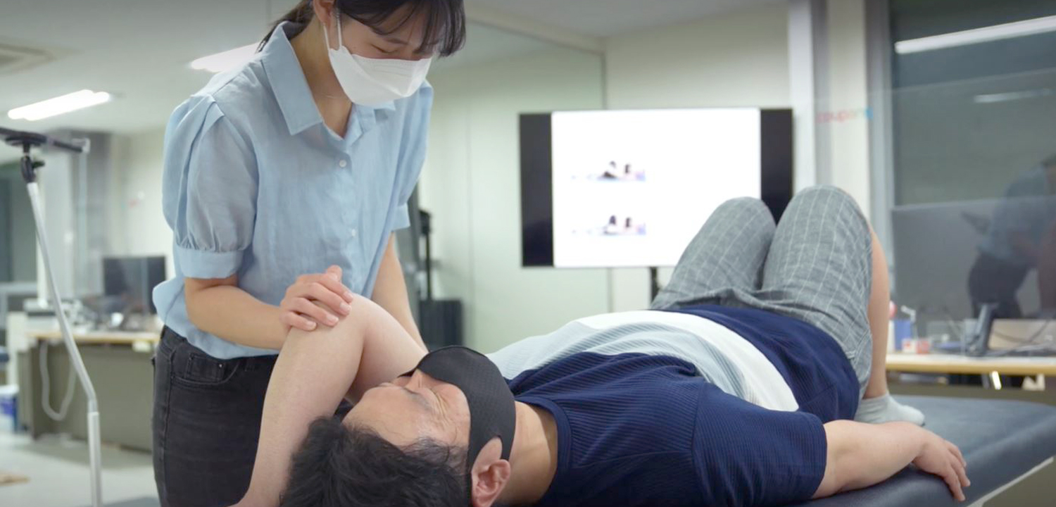 마스크를 쓴 사람이 침대에 누워 있는 사람을 바라보고 있다