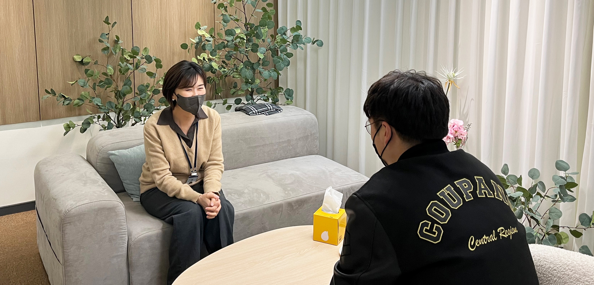 a person sitting on a couch with a person wearing a mask