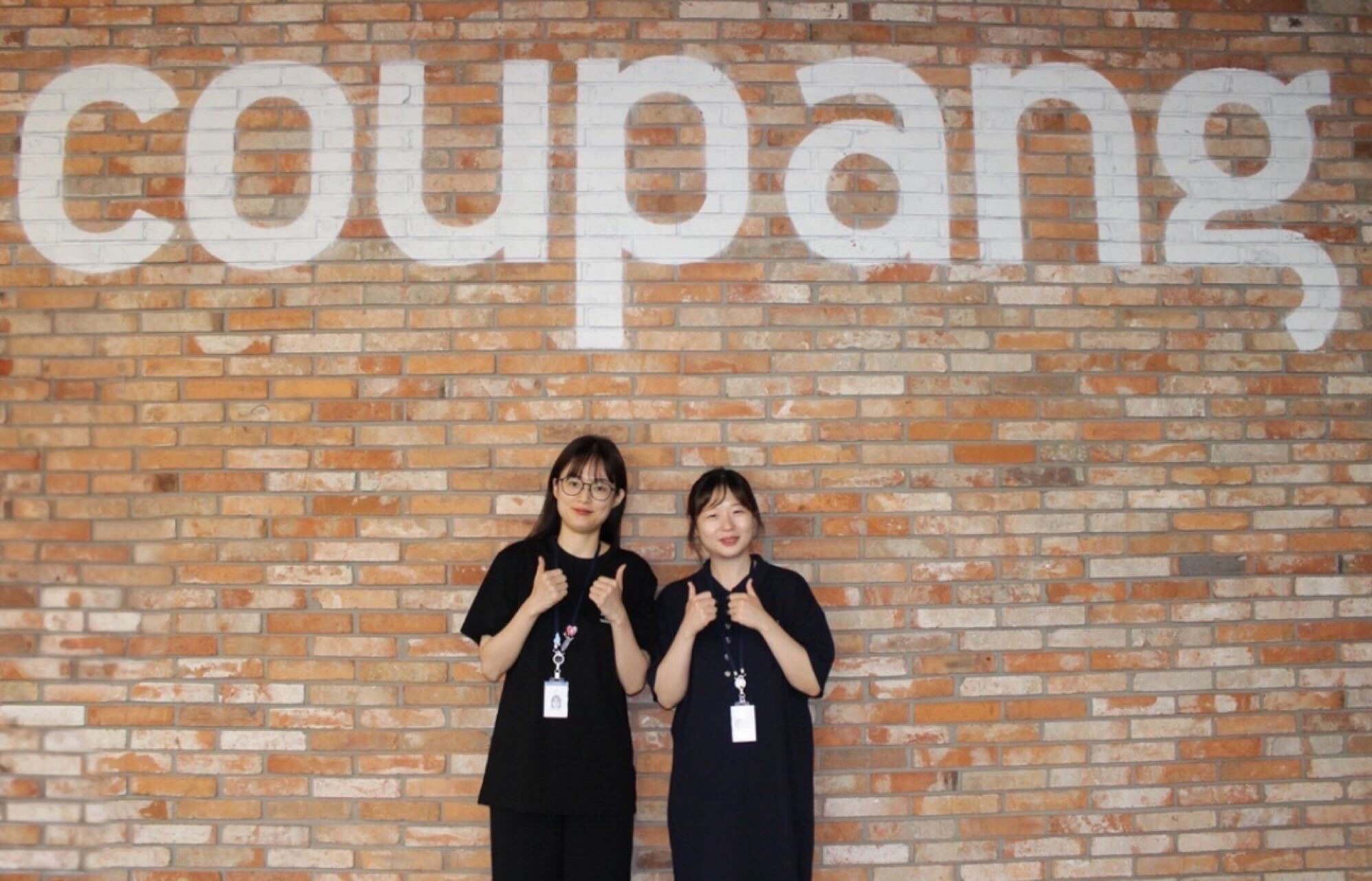 벽돌 벽 앞에 서 있는 두 명의 여성