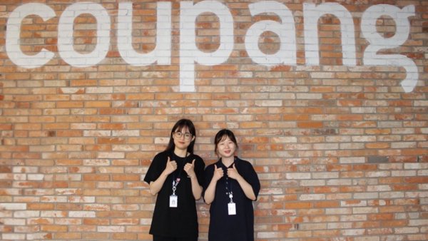 벽돌 벽 앞에 서 있는 두 명의 여성