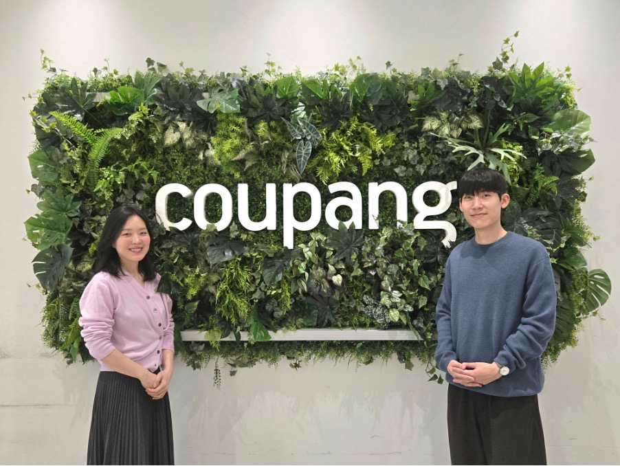 한 사람과 한 사람이 초록 벽 앞에 서 있다