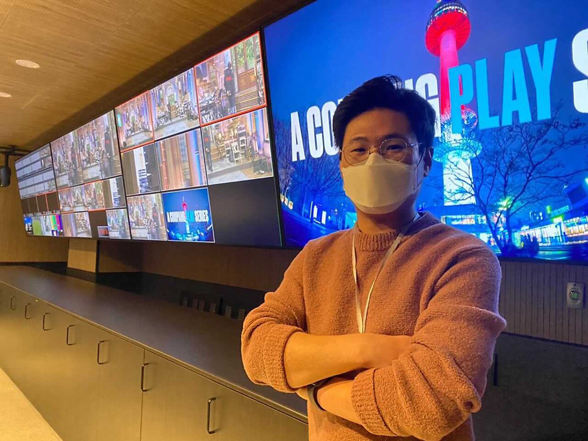 마스크를 쓴 사람이 대형 스크린 앞에 서 있는 모습