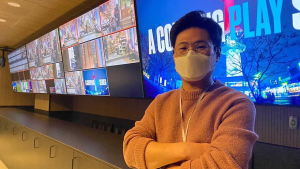 마스크를 쓴 사람이 대형 스크린 앞에 서 있는 모습