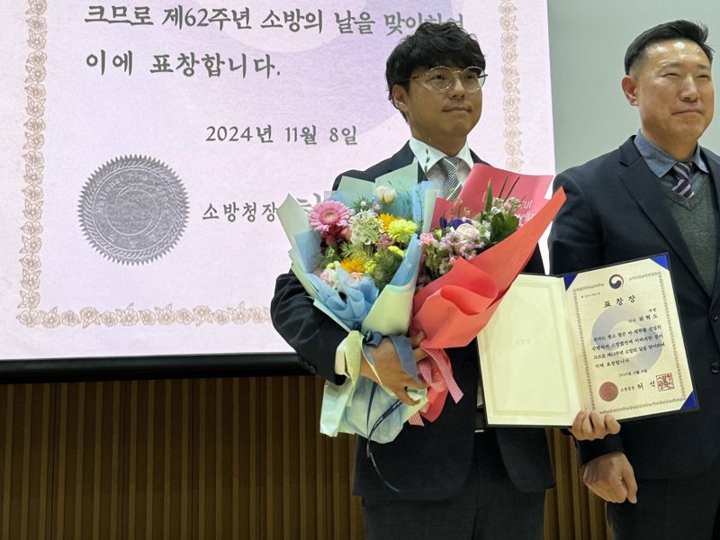 양복을 입은 사람이 꽃과 책을 들고 있습니다