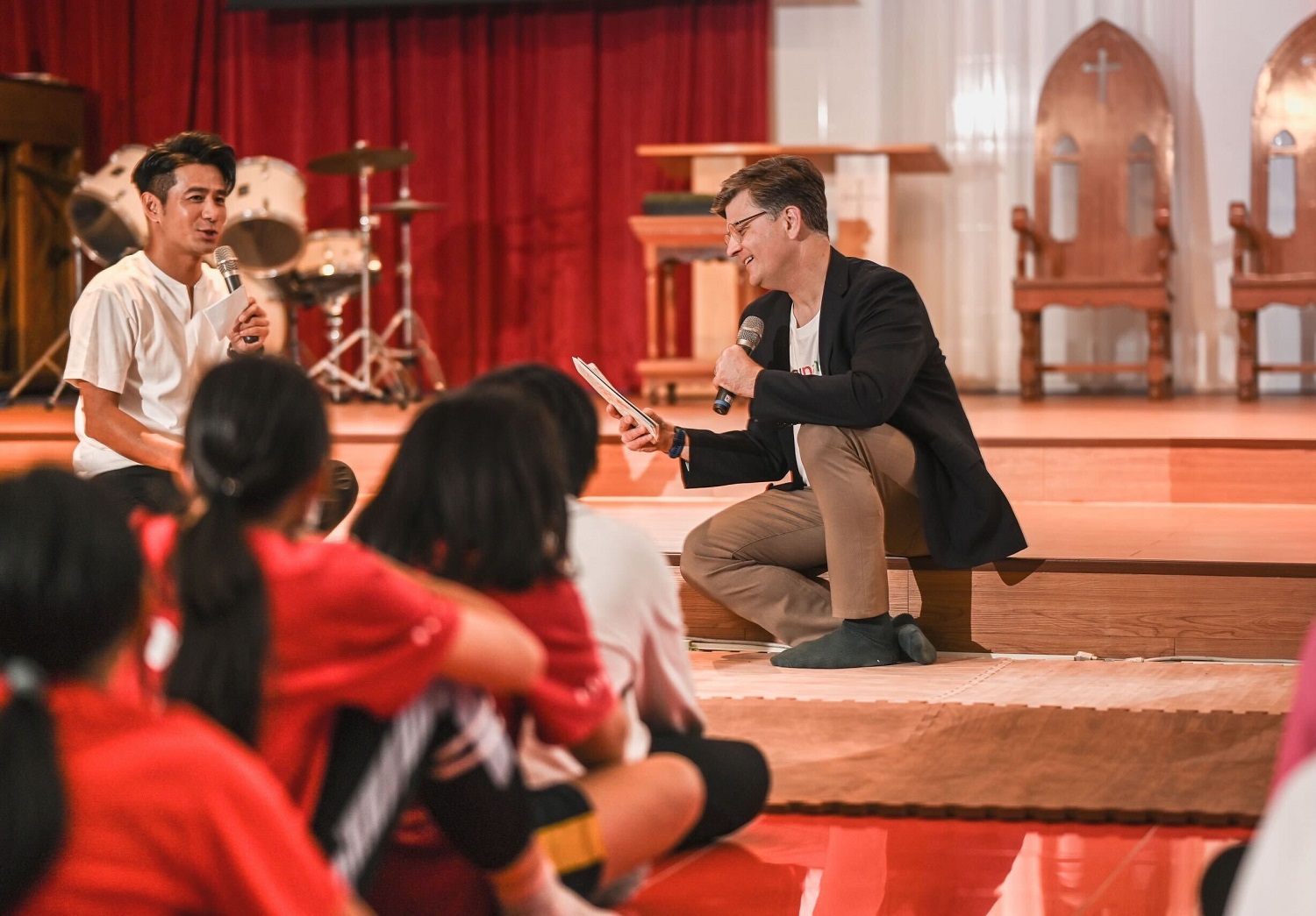 마이크를 들고 한 무리의 사람들과 함께 무대에 앉아 있는 사람