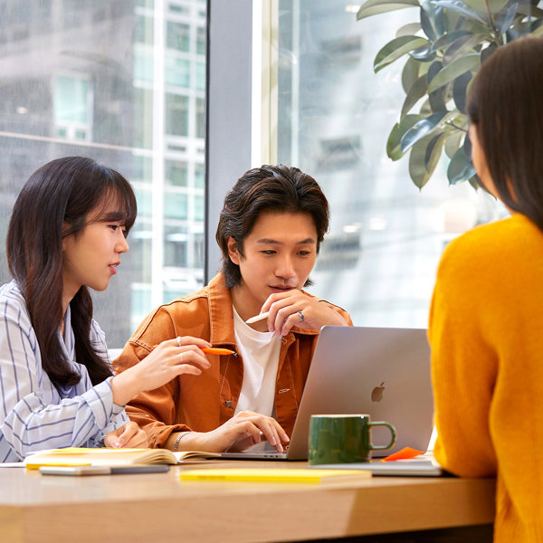 a group of people sitting around a table looking at a laptop