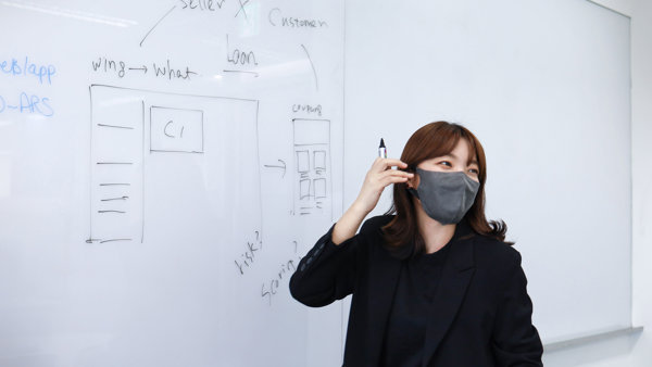 마스크를 착용하고 화이트보드 앞에 서 있는 사람