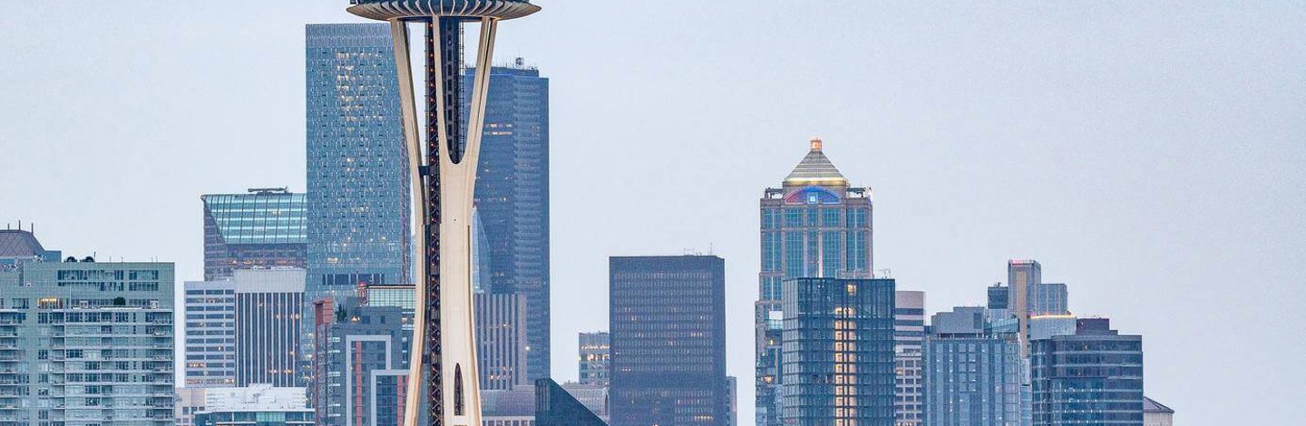 a tall tower with a flag on top with Space Needle in the background