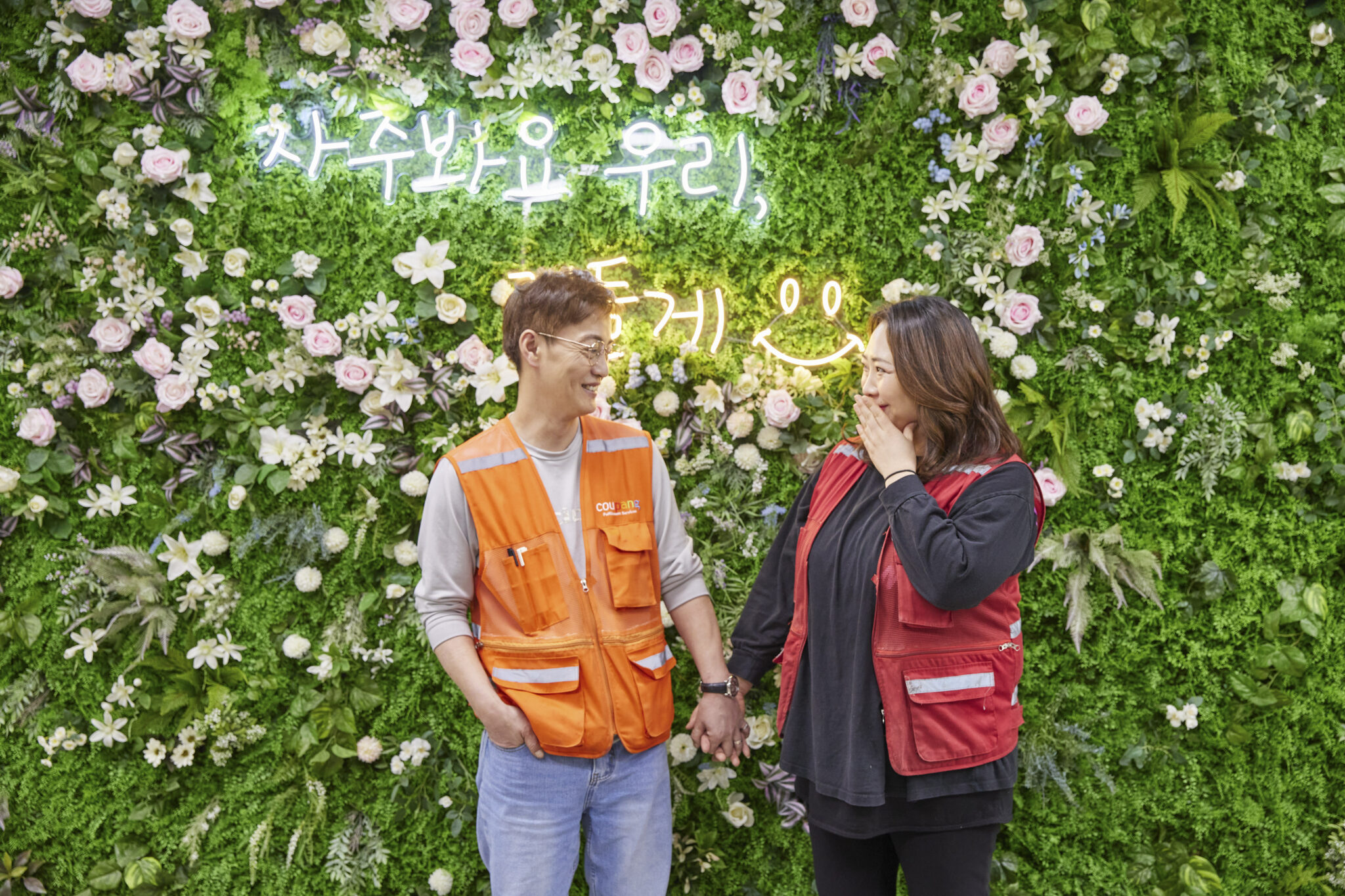꽃 벽 앞에서 손을 잡고 있는 사람과 사람