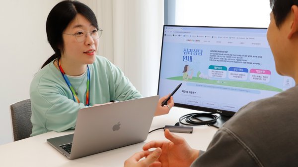 노트북이 있는 테이블에 앉아 있는 사람과 이야기하는 사람