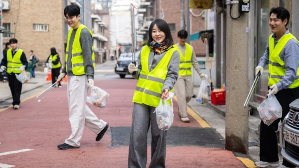 노란 조끼를 입고 가방과 막대기를 들고 있는 사람