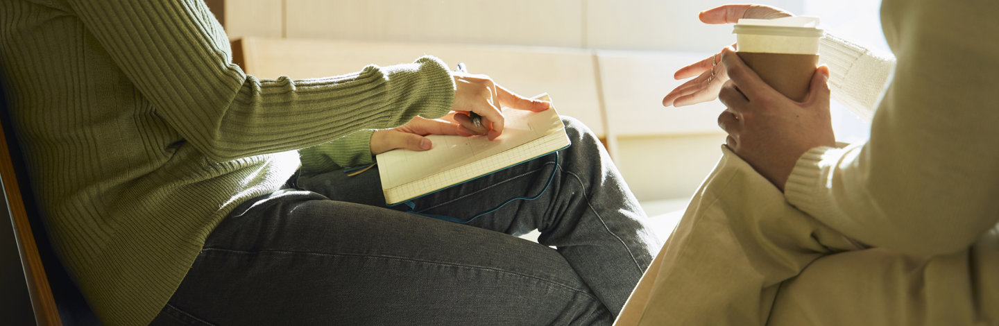 a person sitting on a chair holding a cup of coffee and a notebook