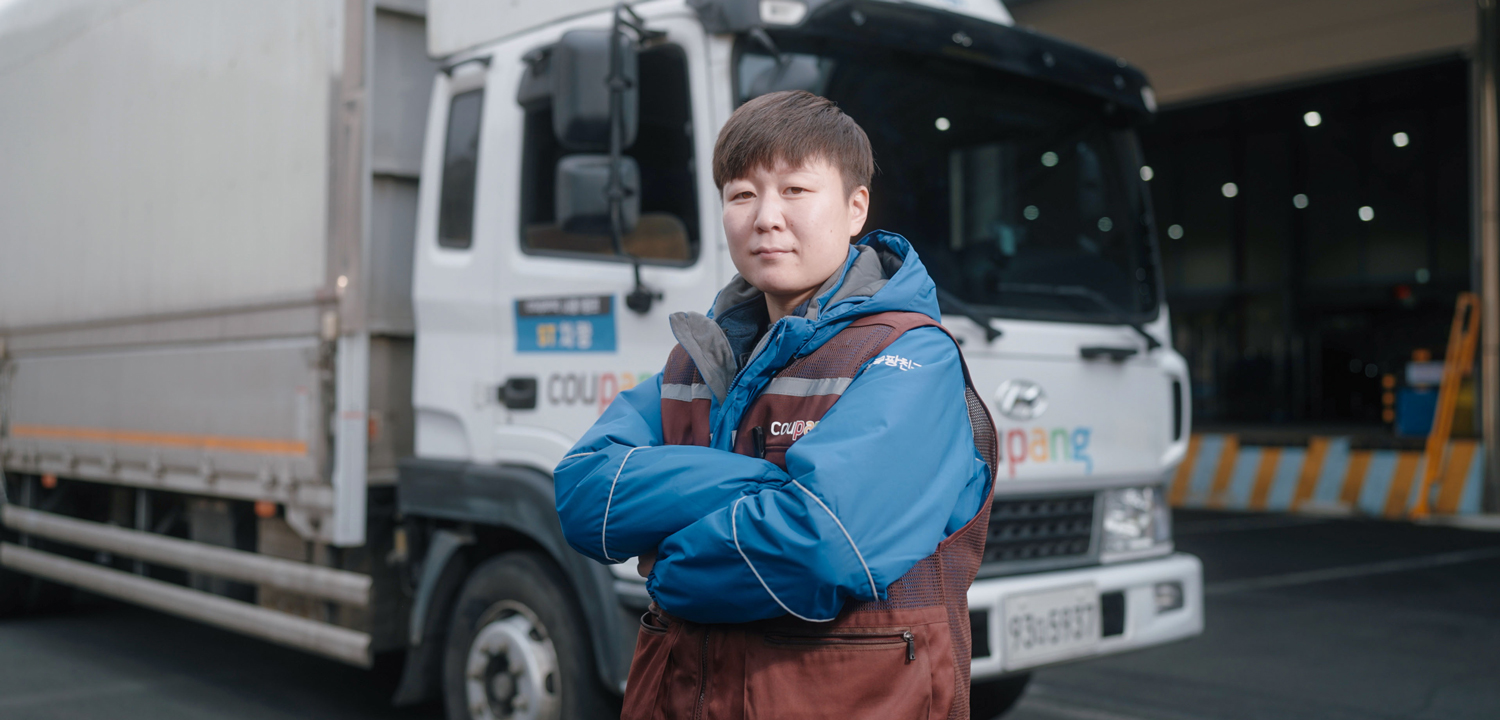 a person in a blue jacket with his arms crossed in front of a truck