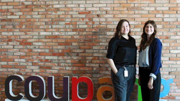 two women standing in front of a brick wall